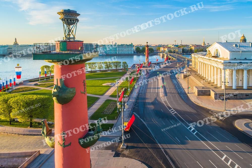 Фотография демонстрирует одну из Ростральных колонн на Стрелке Васильевского острова в Санкт-Петербурге. Колонна смотрит на Неву, вдалеке виднеется Зимний дворец. Это место является одной из наиболее узнаваемых достопримечательностей Северной столицы России и популярным местом для туристов. Изображение подойдет для туристических проспектов, исторических обзоров, культурных публикаций и в качестве рекламного материала для туристических агентств.